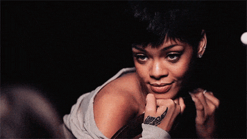 Celebrity gif. Rihanna, with her chest leaned against the back of a chair, smiles before squinting her eyes closed happily.
