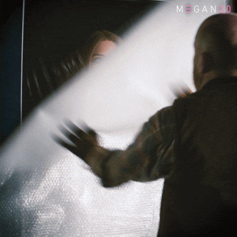 Sponsored gif. Haunted doll Megan escapes from her box and tackles a man to the ground.