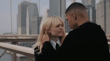 TV gif. On a bridge with a cityscape behind them, Emily Alyn Lind as Audrey on Gossip Girl goes in for a kiss with Evan Mock as Max.