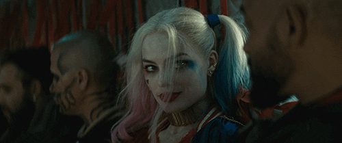 Movie gif. Margot Robbie as Harley Quinn in Suicide Squad looks over and winks at Will Smith as Deadshot.