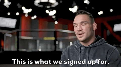 Video gif. Michael Chandler on The Ultimate Fighter sitting for in an interview shrugs and says, "This is what we signed up for."