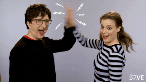 TV gif. Paul Rust as Gus and Gillian Jacobs as Mickey in Love. They have their jaws open in a wide smile as they stare at us but give each other a high five, slapping hands very quickly together.