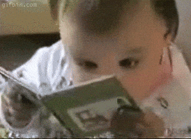 Video gif. Baby holding a board book like an adult, eyes wide and moving back and forth as if reading.