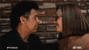 TV gif. Jon Huertas and Mandy Moore as Miguel and Rebecca in This Is Us kiss affectionately.