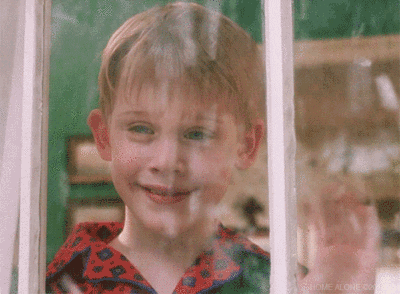 Movie gif. Macaulay Culkin as Kevin from Home Alone waves out a window as snow falls outside.