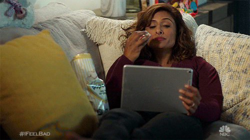 TV gif. Sarayu Blue as Emet in I Feel Bad. She looks incredibly cozy as she lays on a couch and watches something on a huge tablet while shoving popcorn in her mouth.