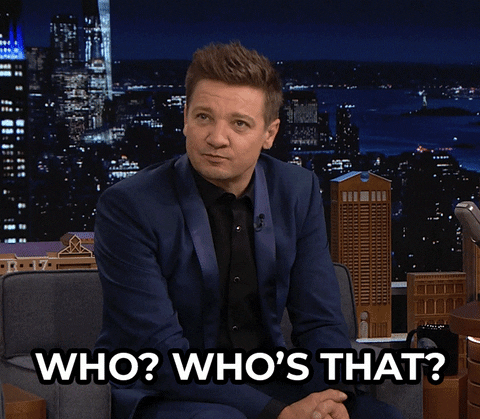 Celebrity gif. Jeremy Renner on the Tonight Show sits in the guest's chair and looks around, saying, "Who? Who's that?"