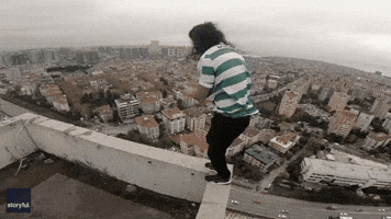 Too Many Layers? Daredevil Removes T-shirt While Keeping Grip on Rooftop Ledge