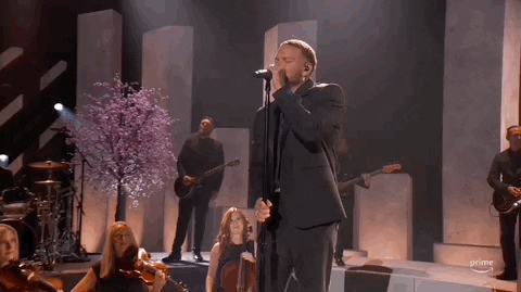 Academy of Country Music Awards gif. On a stage with instrumentalists and cherry blossoms in the background, Kane Brown sings into microphone intently. Brown's eyes start closed before slightly opening them when he finishs singing note with a pleased look