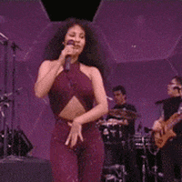 Celebrity gif. Wearing a sparkly eggplant-colored bodysuit, Selena dances cumbia on stage, swinging her hips and smiling wide.