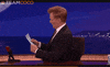Celebrity gif. Talk show host Conan O'Brien looks up from a sheet of paper and pretends like he's shocked to see us. He turns to face us and sets the paper down, saying, "Oh, hello there!"