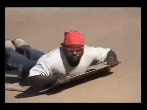 Meme gif. From the Dank Ass Sandboarding Son meme, a man in sunglasses and a red bandanna bodysurfs across a sand dune on a plank, and gives us a thumbs up as he passes us.