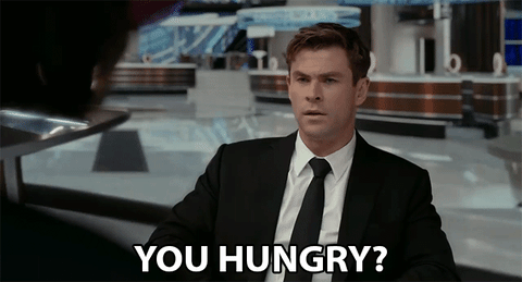 Movie gif. Chris Hemsworth as Agent H in Men in Black International looks sternly and asks, "you hungry?"