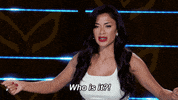 Reality TV gif. Nicole Scherzinger on the Masked Singer, bends her knees slightly, pulling clenched hands in towards her as she shouts in frustration, "who is it?"
