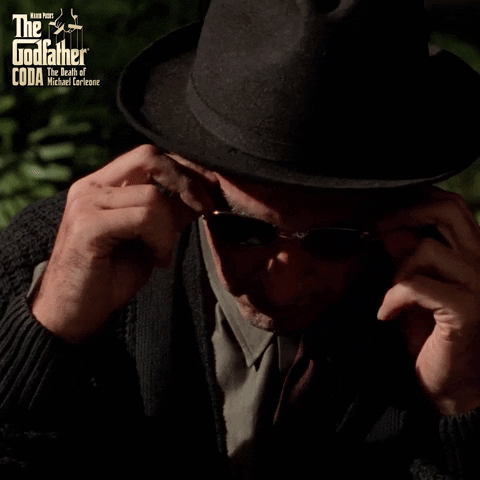 Movie gif. Al Pacino as an elder Michael Corleone in The Godfather Coda, The Death of Michael Corleone, adjusts his sunglasses and looks up slowly.