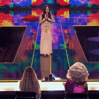 TV gif. A contestant on Queen of the Universe puts her hands together and takes a bow.