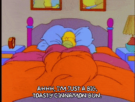 Cartoon gif. From the Simpsons episode "Homer the Heretic", Homer looks positively blissful while snuggled up in bed. Text, "Ahhh, I'm just a big, toasty cinnamon bun."
