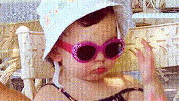 Video gif. A baby wears a hat and sunglasses and she moves to slide the glasses lower and raises her eyebrows, as if she can't believe what she's seeing. She pouts and throws a bit of shade before shoving the glasses back on.