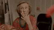 Movie gif. Sitting in front of a cooked turkey with a butcher knife sticking out of it, Cloris Leachman as Josephine on Lez Bomb licks her fingers in enjoyment.