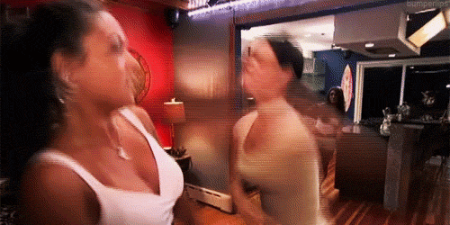 Reality TV gif. Nicole Polizzi and Jenni Farley in Jersey Shore hit each other in a living room and Vinny Guadagnino stands up to stop them.