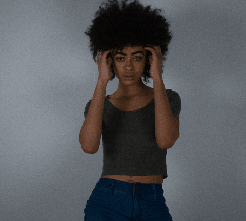 Video gif. A beautiful woman with an afro plays with her hair and gives us a flirty look.