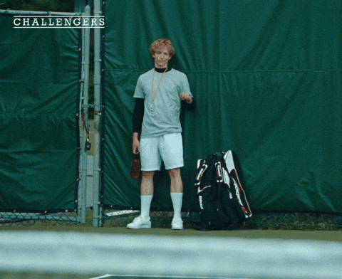 Movie gif. A shot from the movie "Challengers." Art Donaldson and Tashi Donaldson stand on a tennis court. They wave at each other politely. 