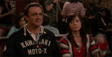 TV gif. Jason Segel as Marshall and Alyson Hannigan as Lily in How I Met Your Mother. They're sitting in a both together and give each other a fat high-five, looking immensely pleased.