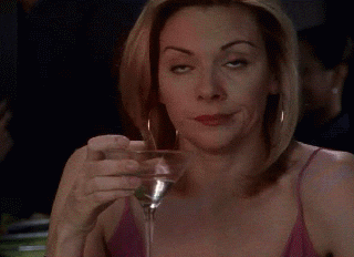 TV gif. Kim Cattrall as Samantha Jones from Sex and the City wears golden hoop earrings and a low-cut fuchsia dress while casually holding a martini glass. She looks completely disinterested, as she rolls her eyes and proceeds to take another sip of her drink.