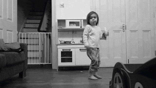 Video gif. A young child chews a bite of a banana as they walk awkwardly across a hardwood floor looking at us. Text, "Oops."