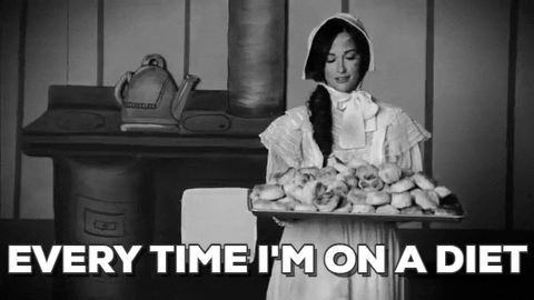 Music video gif. From the video for Biscuits, black-and-white vintage-style clip of Kacey Musgraves wearing a bonnet and prairie dress, holding a pan piled high with biscuits.