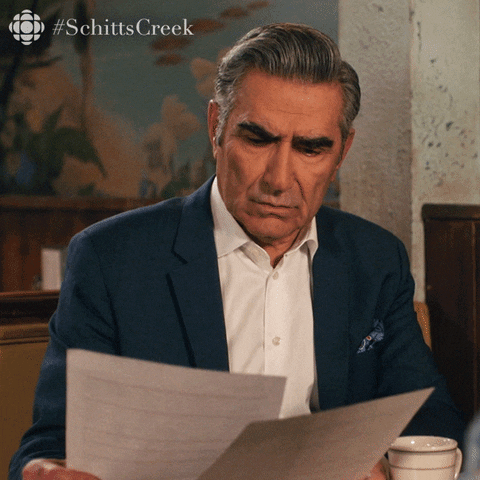 Schitt's Creek gif. Eugene Levy as Johnny looks down at two pieces of paper he’s holding, looking a bit concerned and confused. He looks up with a puzzled and almost disappointed look on his face and asks, “What am I looking at?”