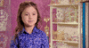 Reality TV gif. Kailia Posey on Toddlers and Tiaras sits in a room full of sparkly, extravagant tiaras. She looks away from us with big eyes and a cheeky smile.