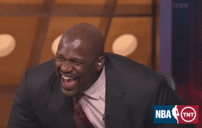 Sports gif. Wearing a dark gray suit jacket, Shaquille O'Neal leans forward in his seat for a prolonged, emphatic laugh.'Neal leans forward in his seat for a prolonged, emphatic laugh.