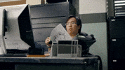 TV gif. SungWon Cho as Joe Furuya in Anime Crimes Division sits at a desk looking at a document, then notices something on the computer screen and waves his colleague over to look at it.