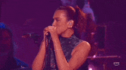 ACM Awards gif. Dua Lipa starts with both hand on the mic as she sings and shakes her head with her eyes closed, before lifting one arm and moving open faced hand in an up and down motion as she continues to sing passionately. 