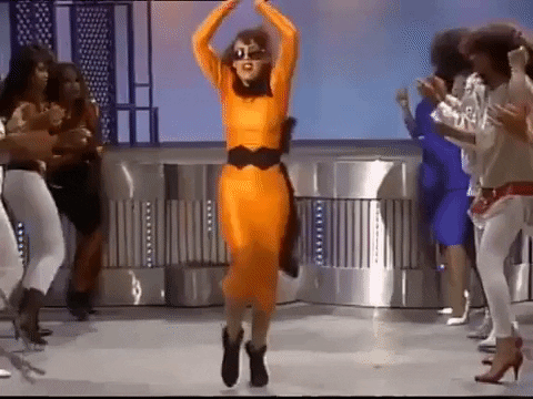 TV gif. Woman on Soul Train is wearing a slinky orange dress and she dances down the walkway, waving her arms and body to the rhythm of the music.