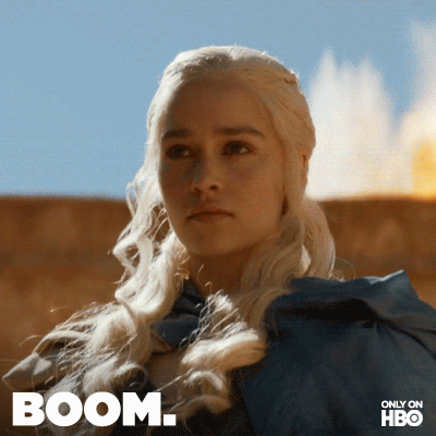 TV gif. Emilia Clarke as Daenerys Targaryen on Game of Thrones has an intimidating and serious expression on her face. Something explodes behind her and flames erupt into the sky, but she remains unphased. Text, “Boom.”