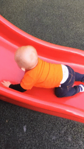 Video gif. A toddler attempts to climb up an orange slide but fails and gives up, lying face first as he slides slowly downward.