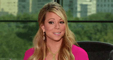 Celebrity gif. Mariah Carey smiles awkwardly while her eyes search around in confusion.