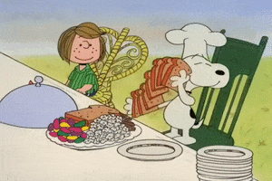 Movie gif. Peppermint Patty and Snoopy in A Charlie Brown Thanksgiving sit next to each at the dinner table. Patty watches as Snoopy, in a chef’s hat, prepares the plates for everyone. He starts by grabbing a stack of bread slices and shuffles them like they are a stack of playing cards then puts two slices on a plate. Patty first appears content but then concerned as she watches Snoopy put different snacks that aren't normal thanksgiving side dishes like popcorn and rainbow candies. He wipes his hands clean like he did a good job and tosses the plate across the table like a frisbee . 