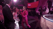 Oscars 2024 GIF. Ryan Gosling, dressed in a Barbie pink tuxedo and sunglasses, puts a microphone in the face of Emma Stone, who grabs it and fervently sings, “I’m just Ken!”
