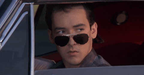 Movie gif. John Cusack as Lane Meyer in Better Off Dead has his car window rolled down and he looks out of it, tilting on his nose. He winks dramatically, moving his mouth open to exaggerate the wink.