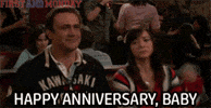 TV gif. Jason Segel and Alyson Hannigan as Marshall and Lily in How I Met Your Mother sitting together in their booth smirk as they high five in perfect unison. Text, "Happy Anniversary, Baby."