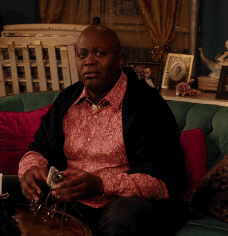 TV gif. Tituss Burgess as Titus Andromedon from Unbreakable Kimmy Schmidt sits on a couch, looking worried. He blesses himself with the sign of the cross, then follows up by patting his shoulders, holding up two fingers on each hand, and moving around in a jaunty little dance. Finally, he looks up, kisses his fingertips, and holds up two fingers to the ceiling as if to say a peaceful goodbye. 