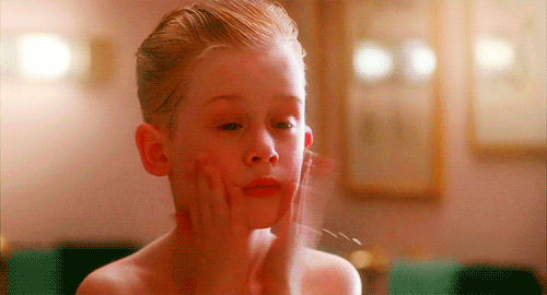 Movie gif. Macaulay Culkin as Kevin in Home Alone slaps aftershave onto his freshly shaven face and screams in surprise.