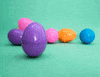 Digital compilation gif. Purple plastic Easter Egg rocks around then cracks open on a pale green surface. Five crocheted bunnies hop out, each a different color.