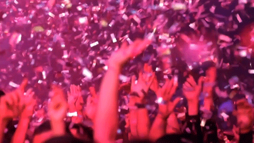 Video gif. Hands reach up in the air at a nightclub as confetti flies down around them.