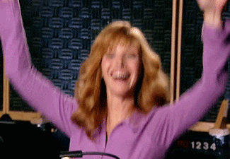 TV gif. Lisa Kudrow as Valerie in The Comeback jumps up in down with her hands in the air above her head, grinning in excitement.