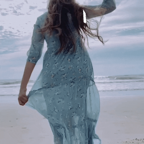 Video gif. A woman wearing a summer dress and hat is running towards the waves at the beach. It goes into slow motion as she takes her hat off and continues running. Text, "Let's gooooo!"