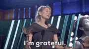 Celebrity gif. Smiling on stage, Renee Zellweger brings a hand to her stomach and says, “I'm grateful.”